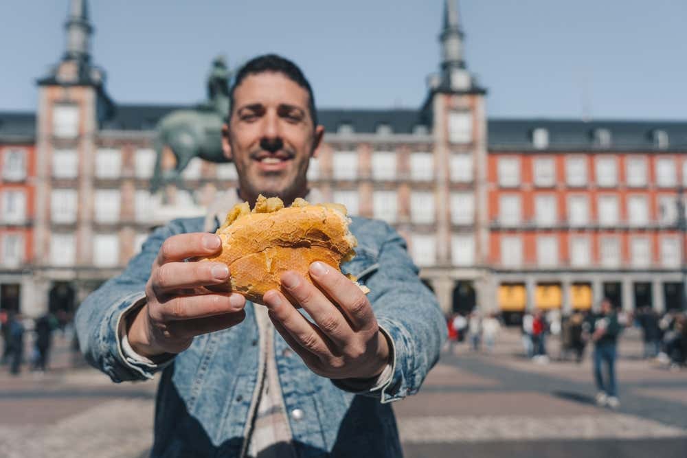 A man holding a calamari sandwich in Plaza Mayor, Madrid.