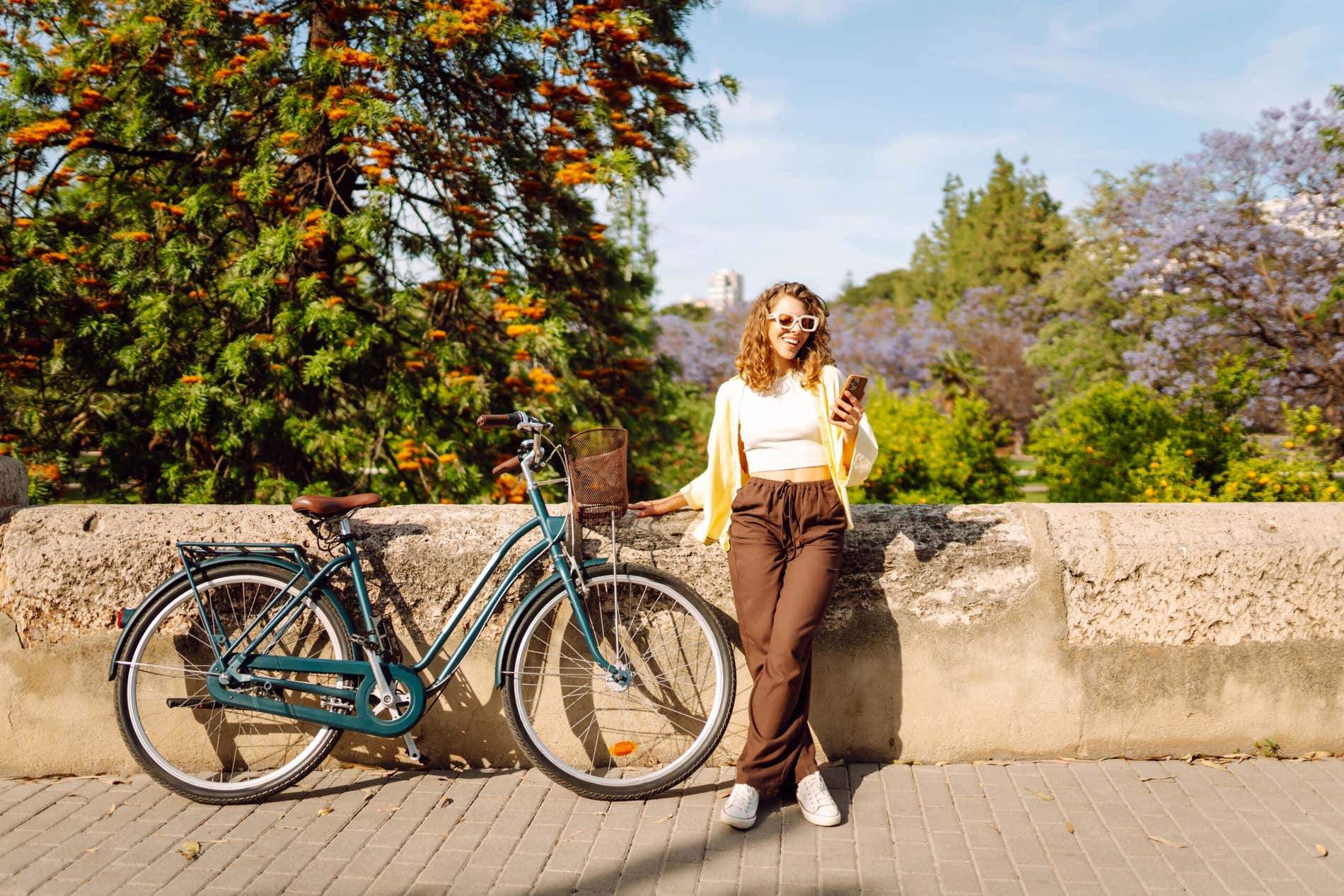 A cheerful tourist holding a phone rides a bike on a sunny day in the park.