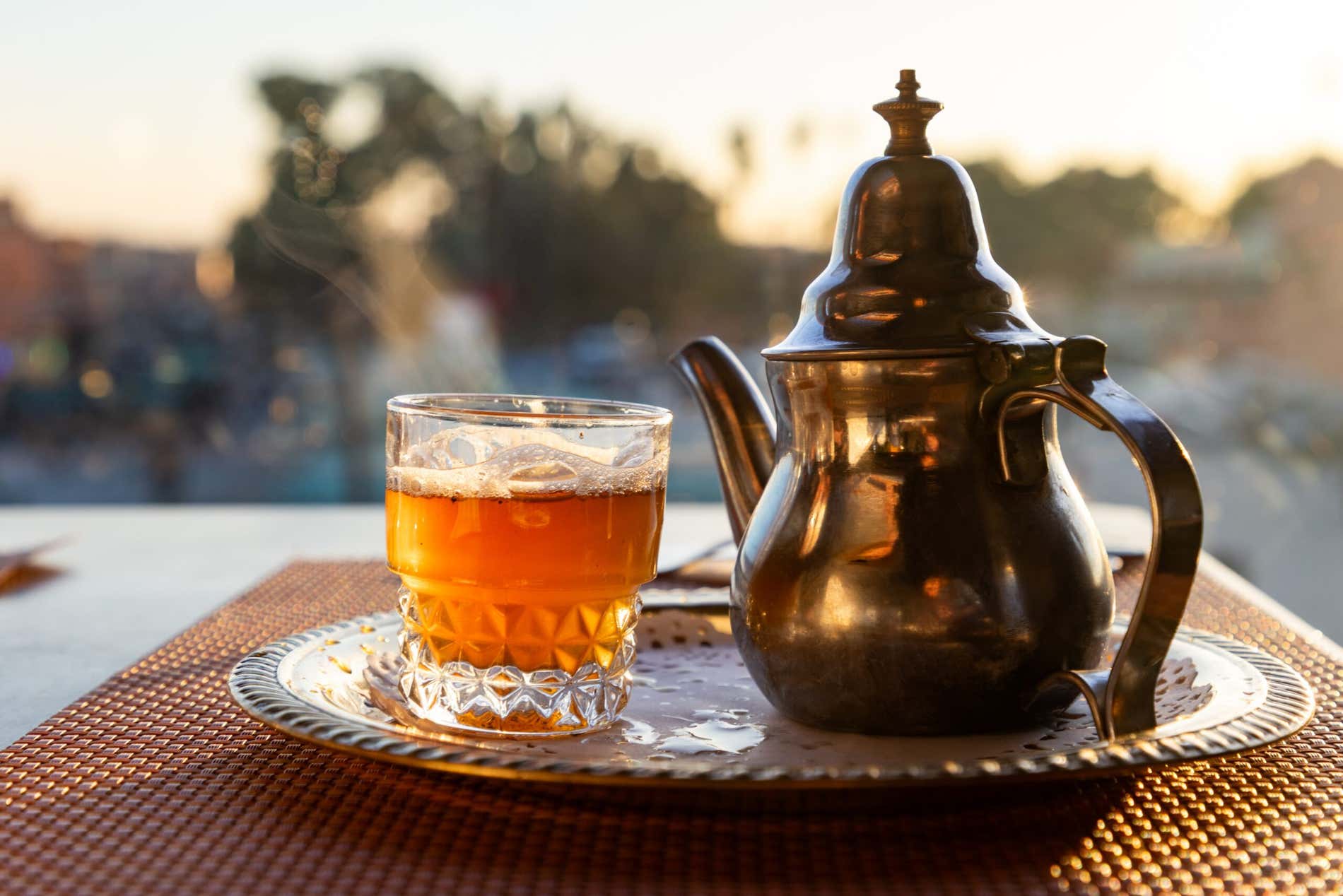 Un piattino con sopra una teiera di accaio e un bicchiere di tè