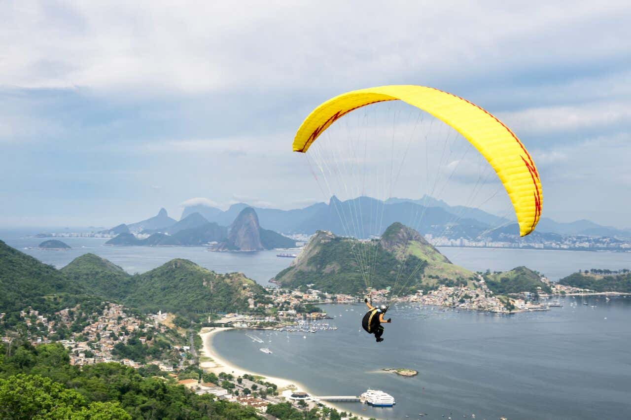 Parapente amarelo brilhante sobrevoando o horizonte montanhoso da cidade, visto de um parque na encosta em Niterói