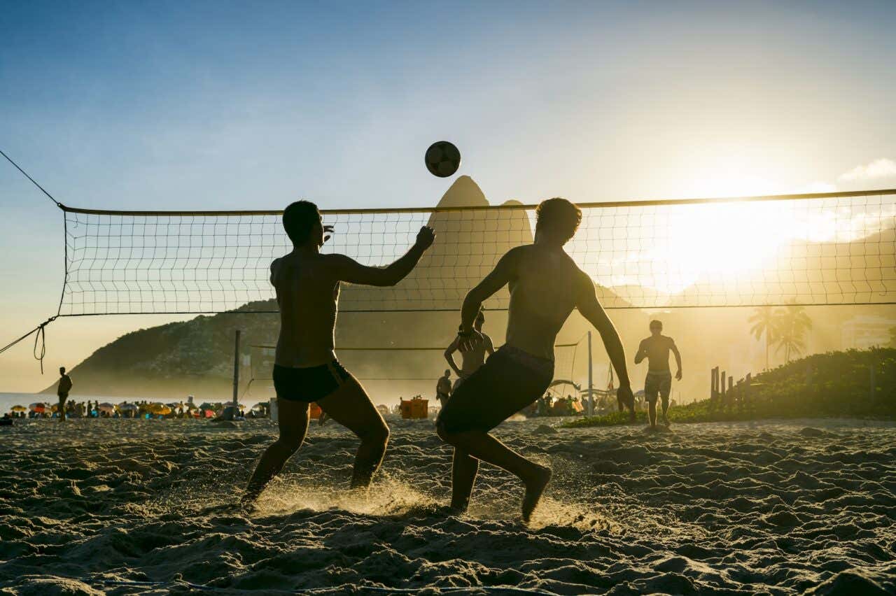 Silhuetas de brasileiros jogando futvolei com o pôr do sol da Montanha dos Dois Irmãos como pano de fundo na Praia de Ipanema, Rio de Janeiro, Brasil