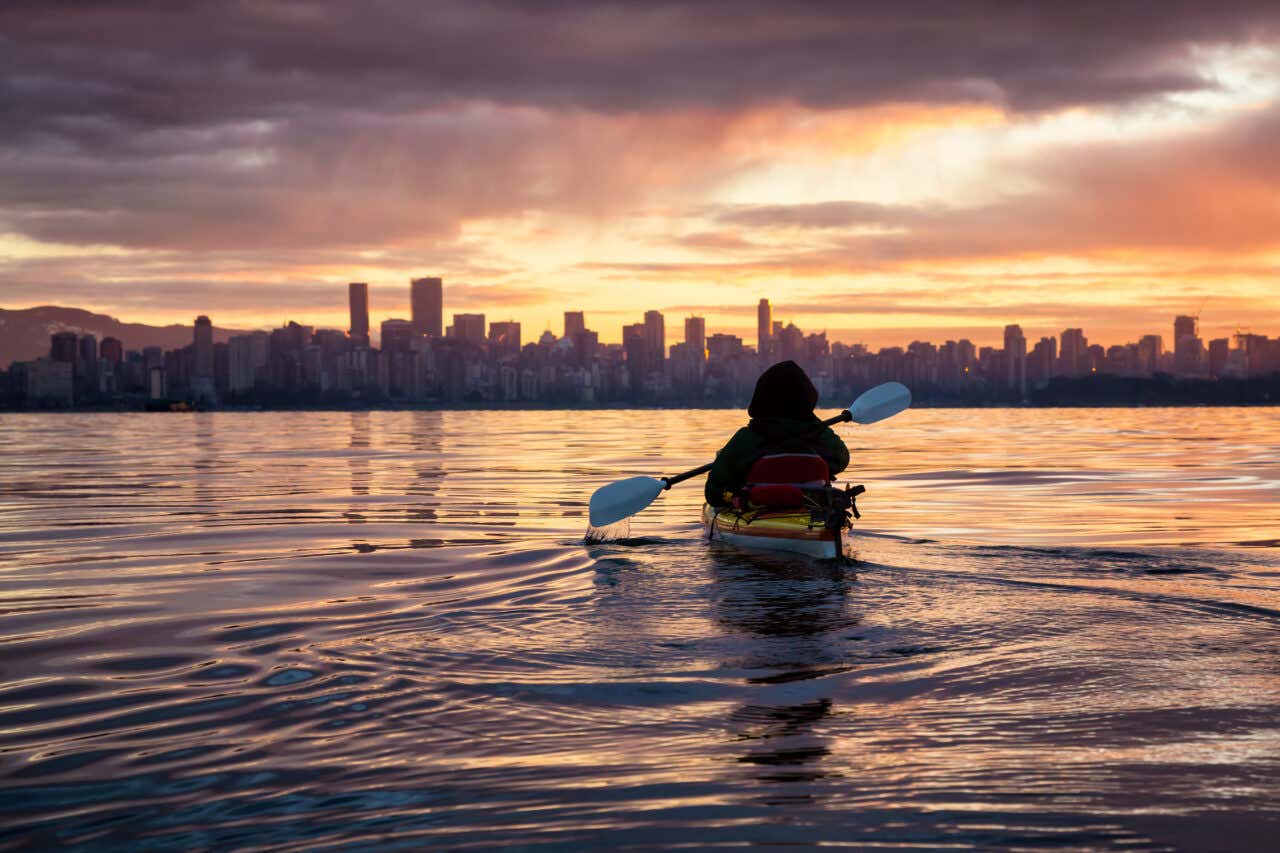 Personne faisant du kayak avec la ville de Vancouver en fond au coucher de soleil
