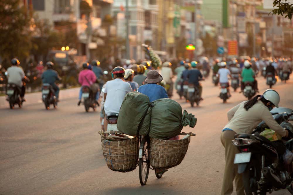 Traffico urbano di Ho Chi Minh, una strada trafficata con persone in bici e in moto in mezzo agli alti edifici moderni alla luce tenue del tramonto