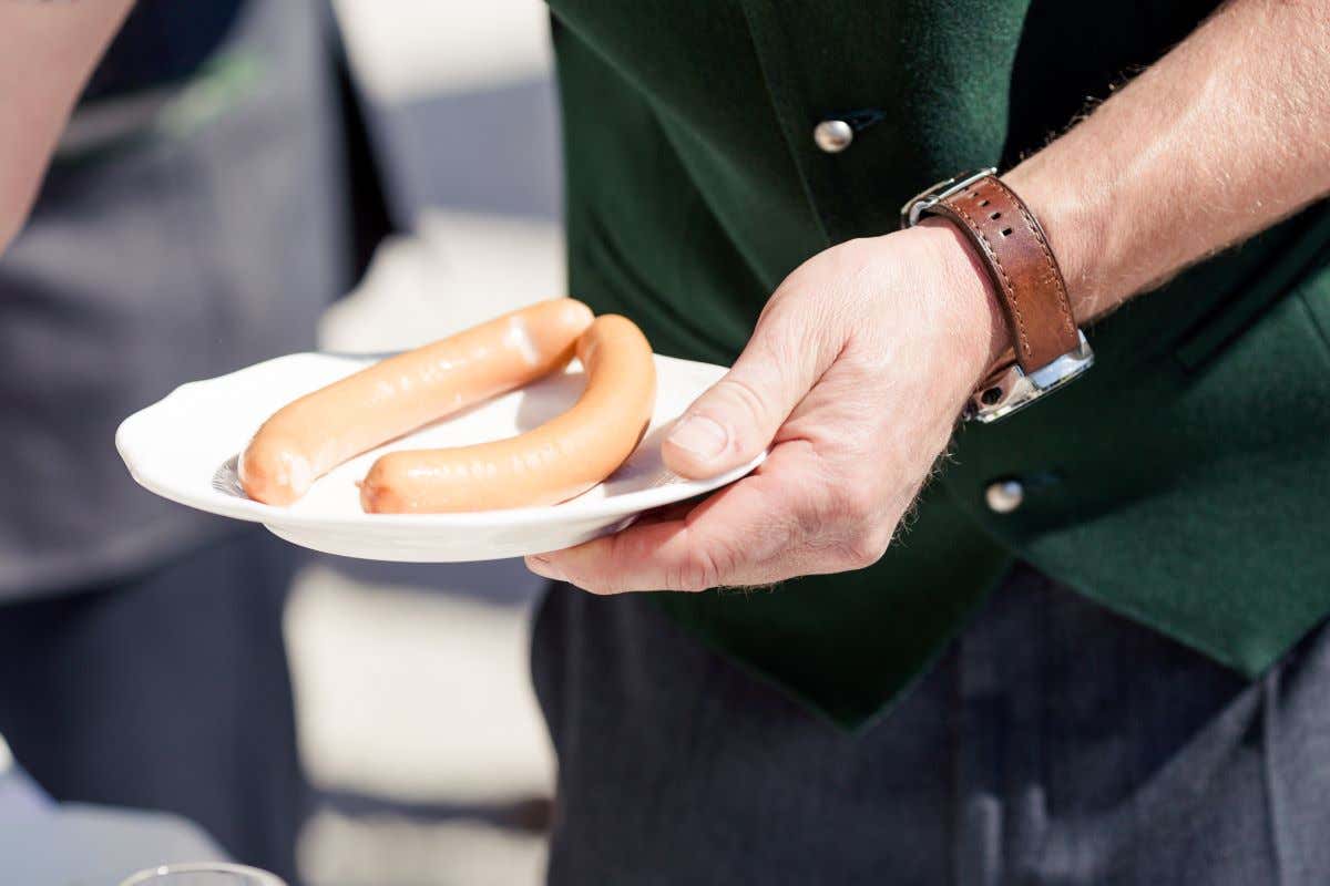 Detalle de una mano que sujeta un plato con dos salchichas vienesas