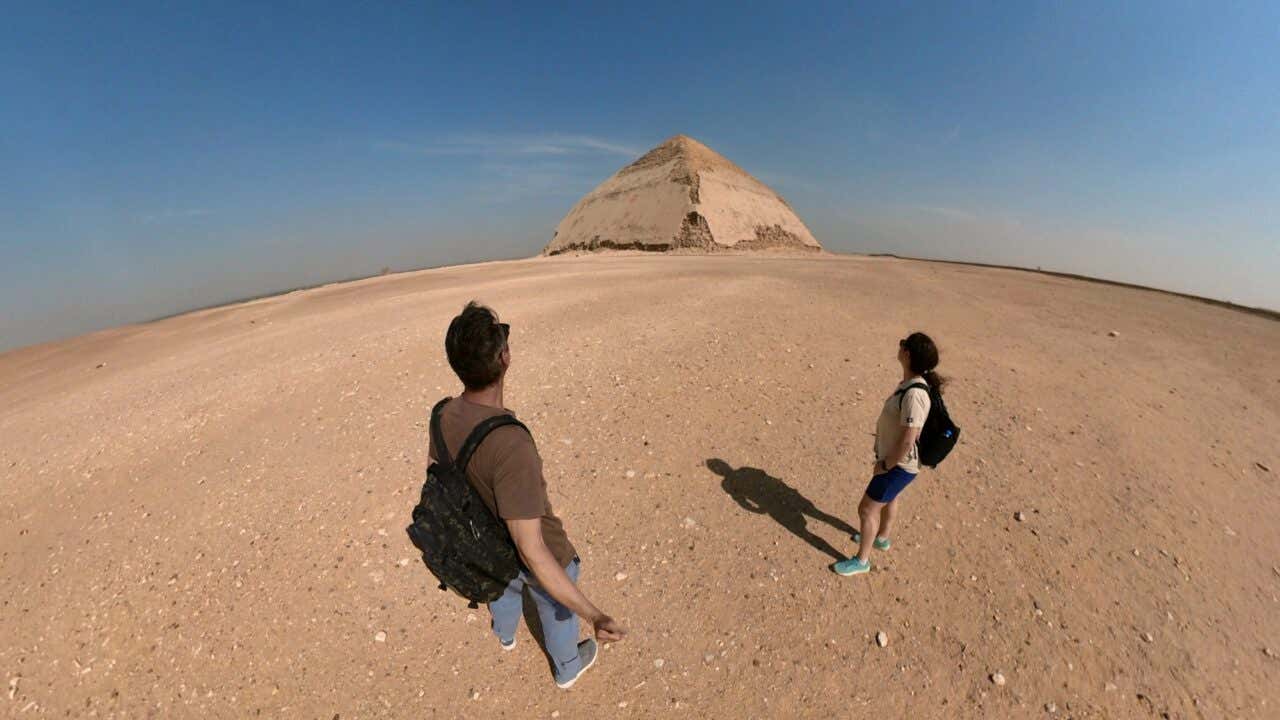 Un hombre y una mujer mirando a una pirámide en la distancia, la Pirámide Acodada, en Egipto.