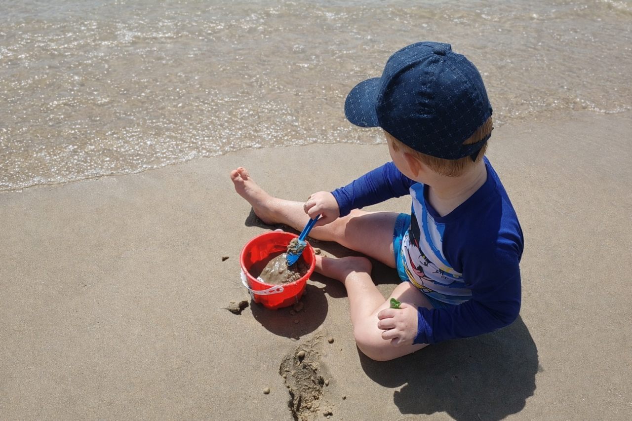 Um menino brincando com a areia da praia enquanto observa o mar