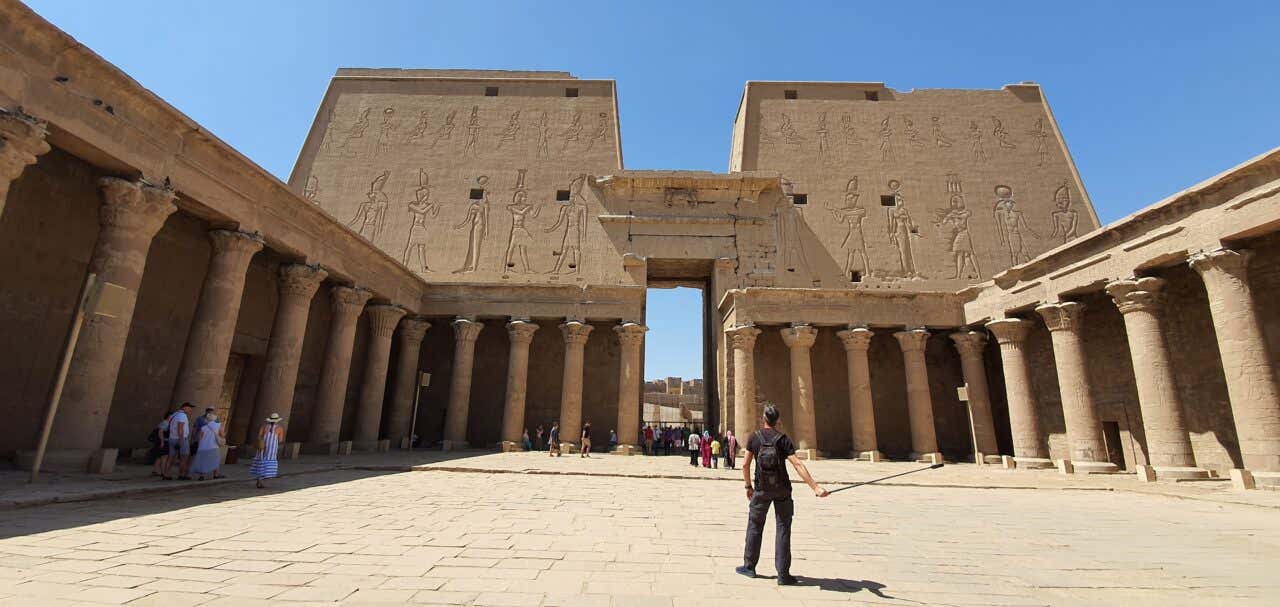 Un hombre delante de la portada monumental y columnas del Templo de Edfu.