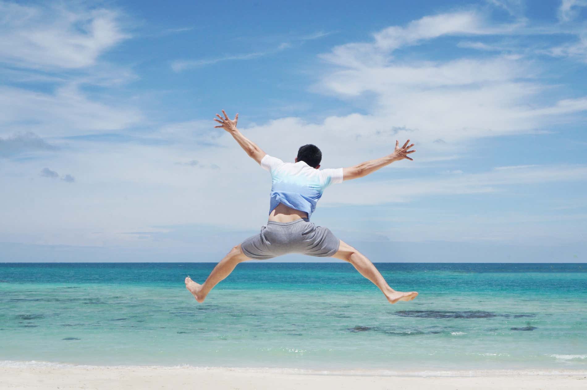 Homem dando um pulo em uma praia de águas cristalinas