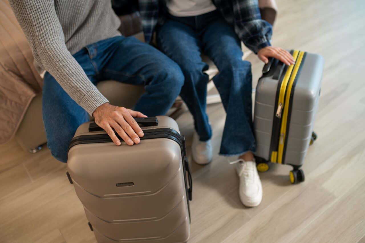 Duas pessoas segurando duas malas sentados em um sifá