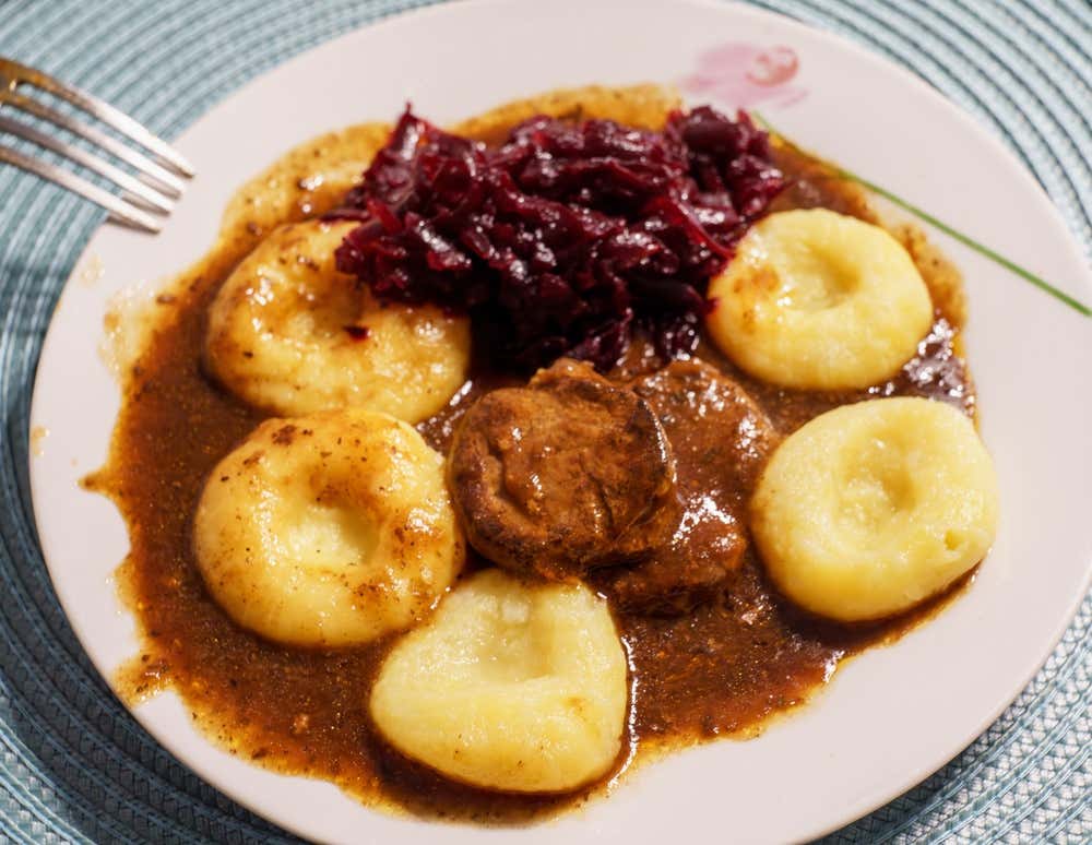 Piatto piano contenente un secondo tradizionale polacco: bocconcini di carne in denso sugo scuro, affiancati da kluski śląskie (gnocchi di patate rotondi con fossetta centrale) e un contorno di cavolo rosso stufato