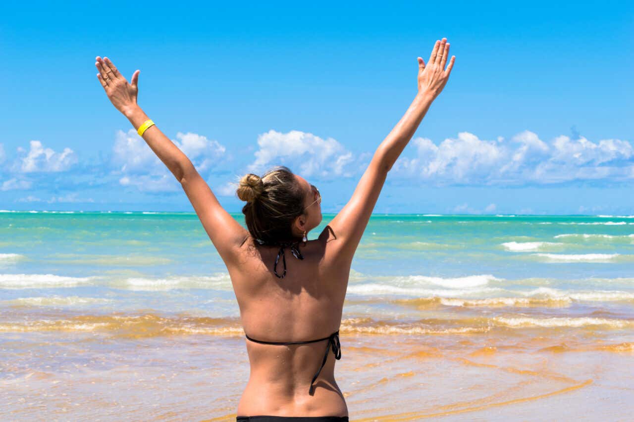 Uma mulher levantando os braços em uma praia de Maragogi