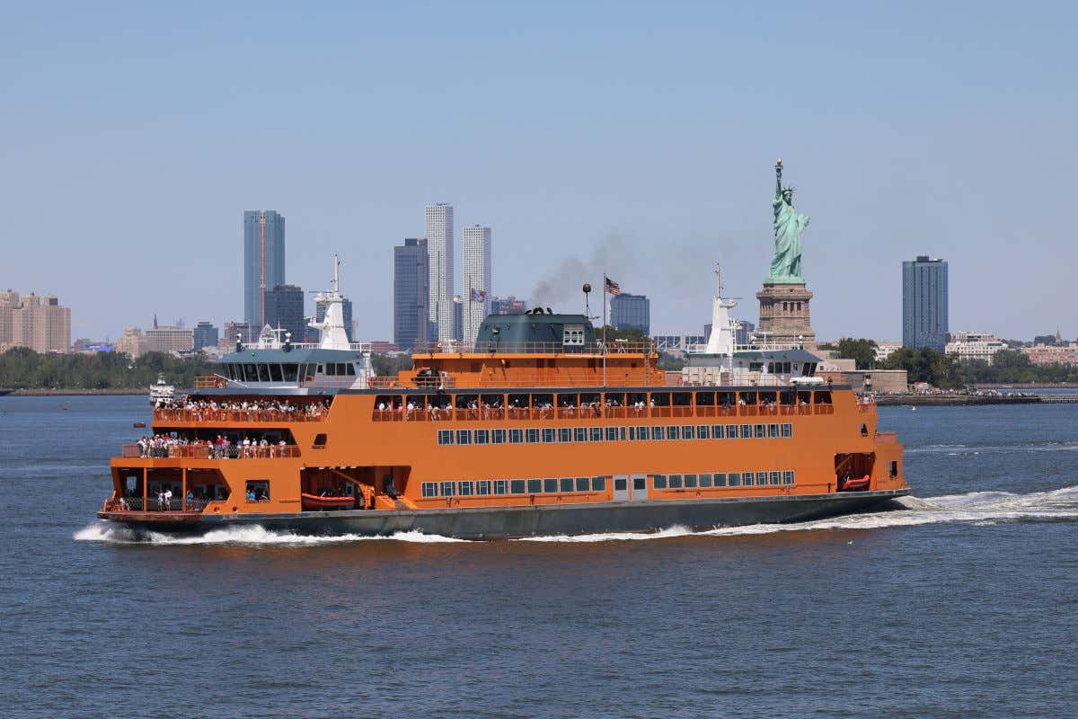 El ferry de Staten Island, de color naranja, navegando por Nueva York junto a la Estatua de la Libertad