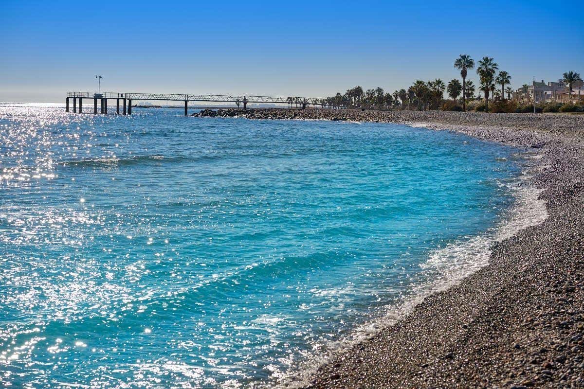 Aguas azules claras y bahía de piedras en un amanecer en la costa de Castellón con palmeras al fondo