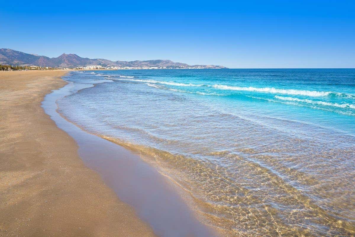 Aguas cristalinas bañando una bahía de arena dorada con montañas al fondo