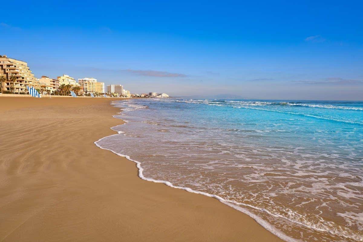 Playa vacía de arena dorada con edificios altos en Castellón