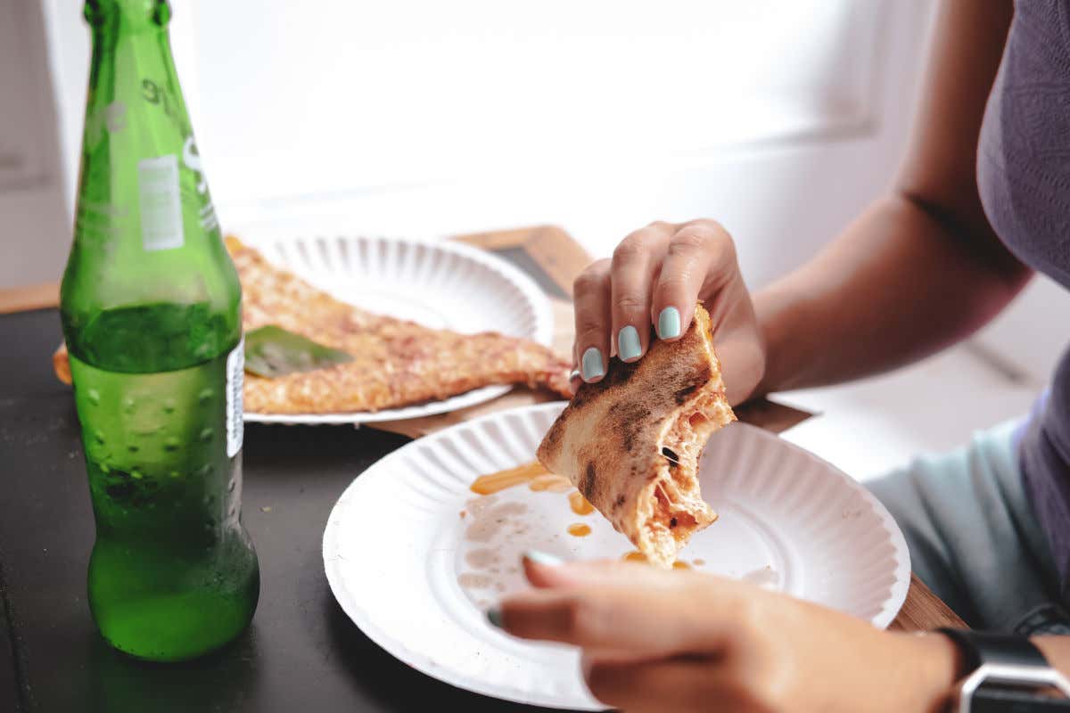 Unas manos cogiendo una porción de pizza de grandes dimensiones en un plato de papel