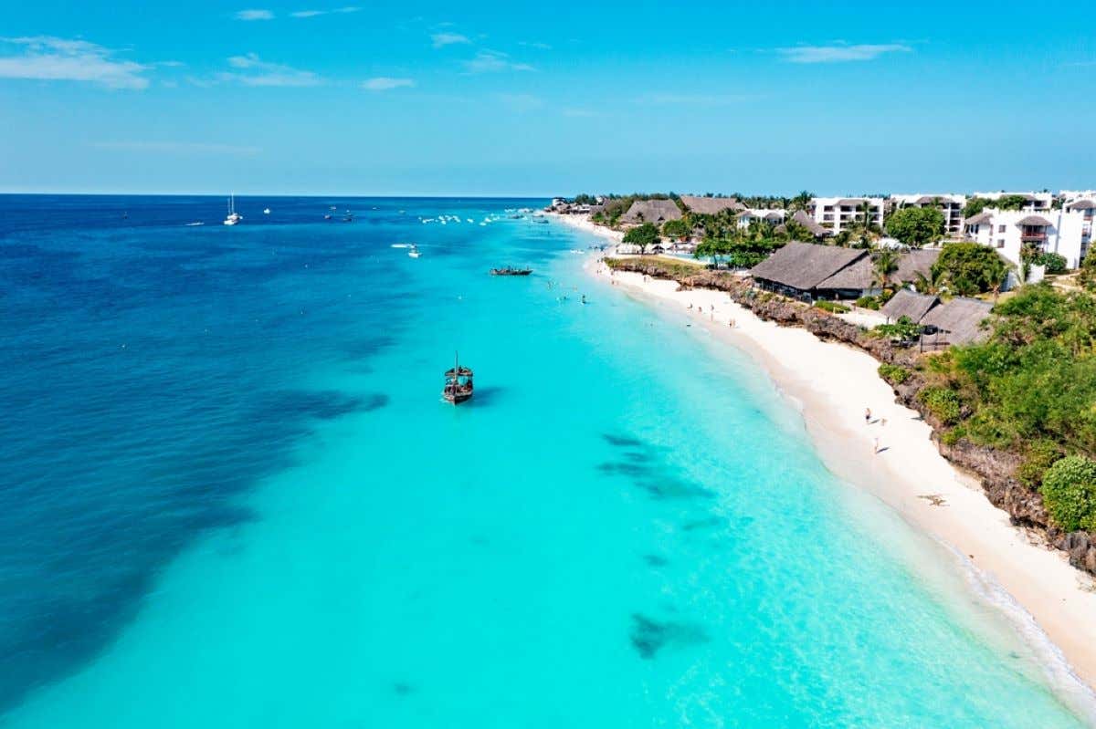 Vistas aéreas de un barco navegando en las aguas turquesas de Nungwi con una playa de arena blanca.