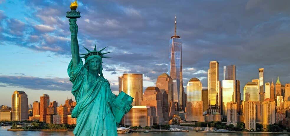Statue of Liberty at sunset with skyscrapers in the distance in New York.