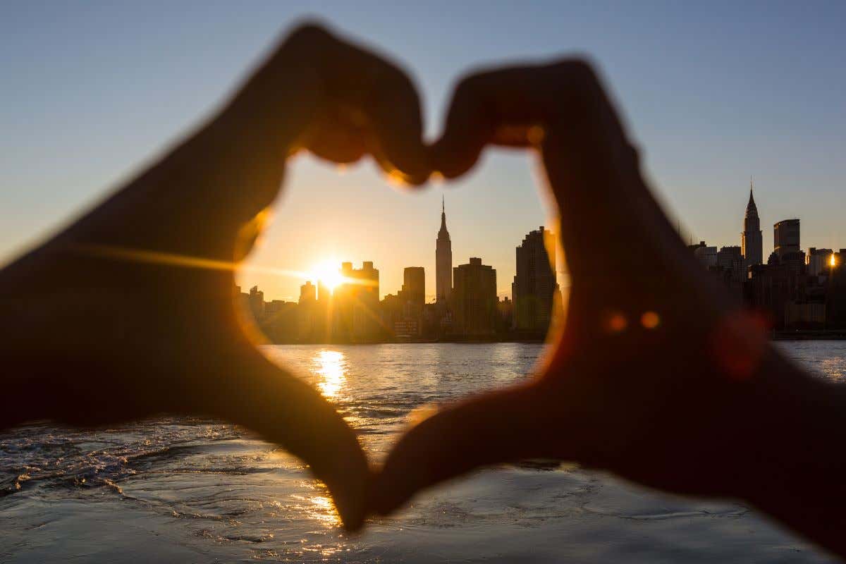 Manos formando un corazón con el perfil urbano de Nueva York de fondo