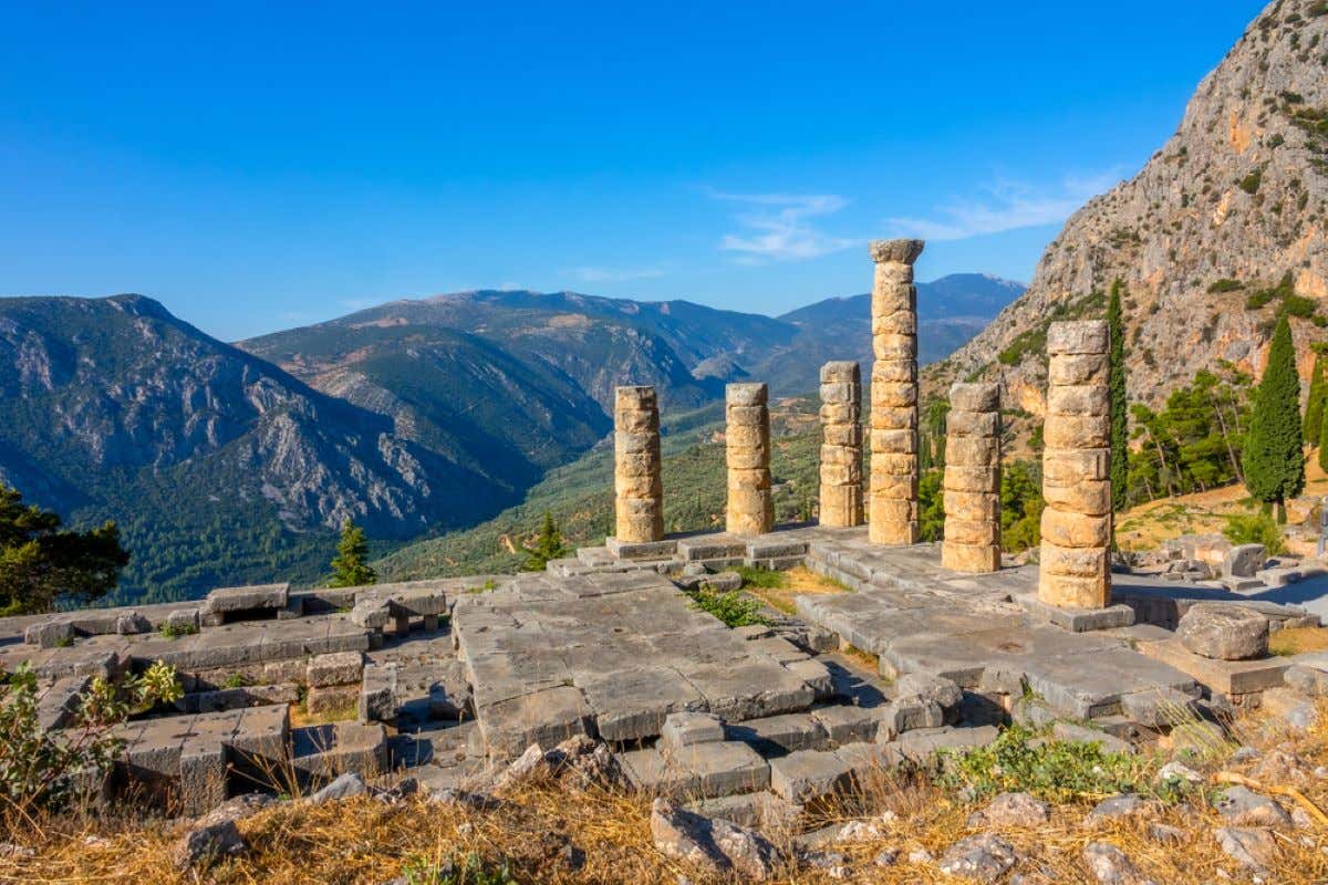 Ancient ruins of Delphi with sunny mountains and a blue sky in the background.