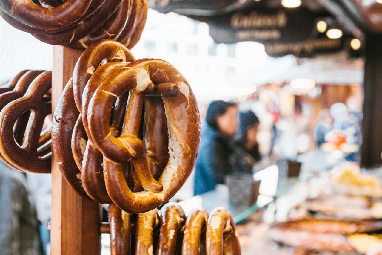 Varios pretzels grandes y dorados colgados de un soporte de madera en una feria al aire libre.