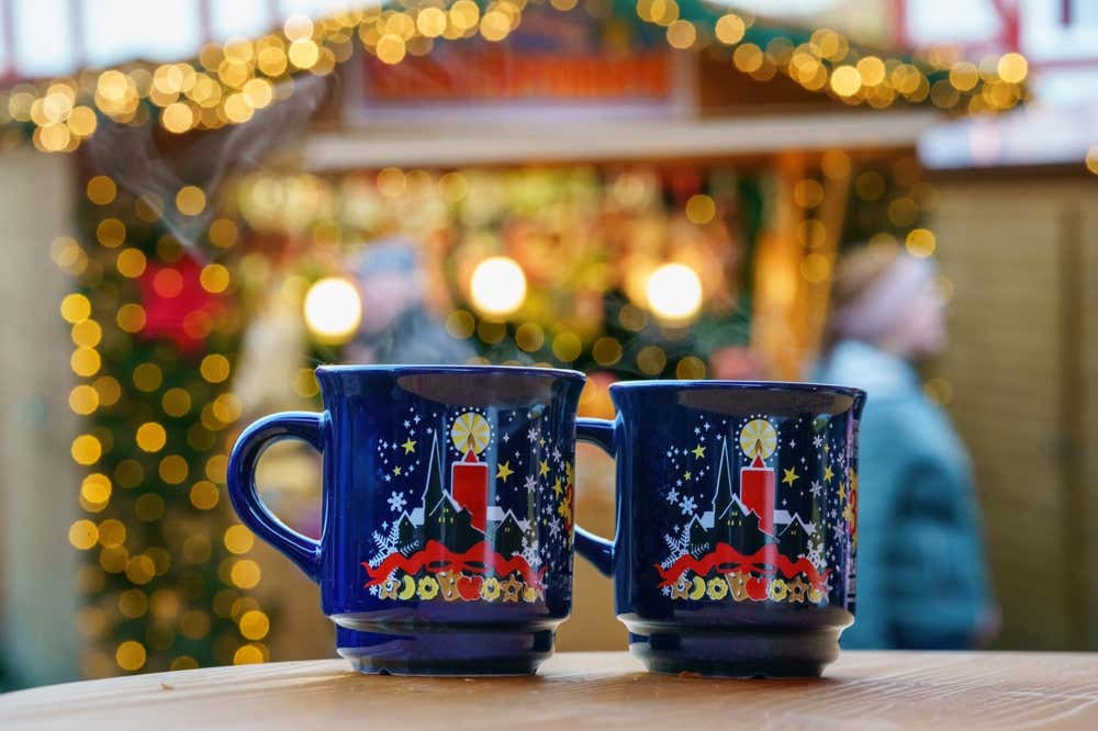 Dos tazas de Glühwein, el vino caliente de Alemania en un mercadillo de navidad con luces desenfocadas en segundo plano