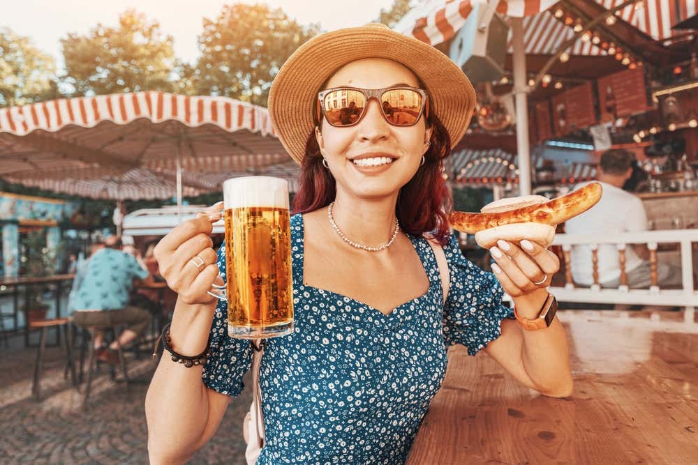 Mujer con sombrero, con una cerveza y una bratwurst en la mano en un biergärten
