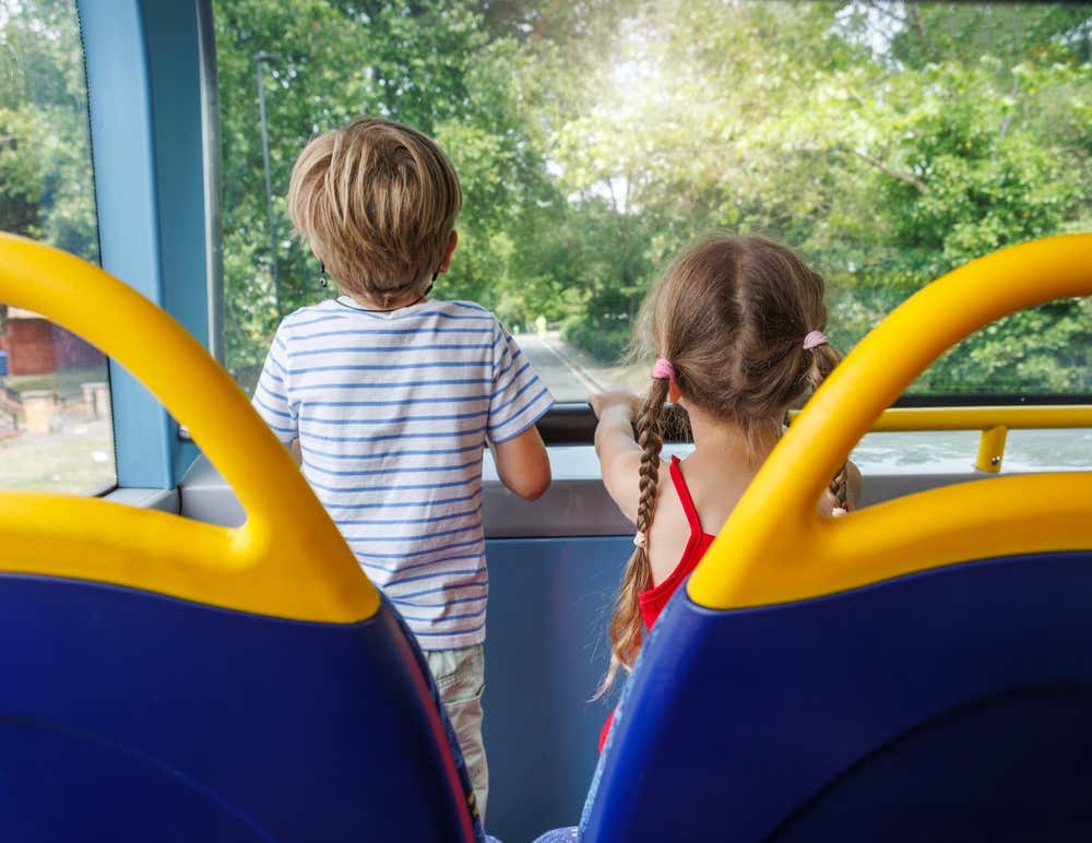 A young boy and girl looking out at the street from the top deck of the sightseeing bus