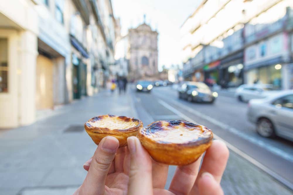 Hands holding two pastéis de Belém on a street in Lisbon
