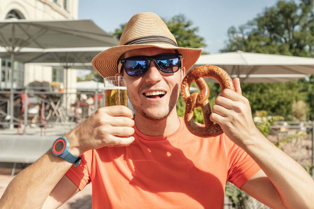 Hombre con gafas de sol y una jarra de cerveza y un pretzel grande en la mano