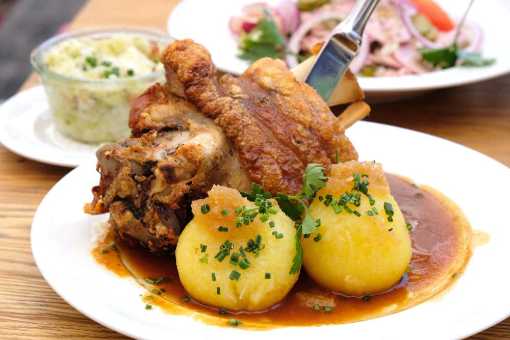 Plato con schweinshaxe (codillo asado) y patatas y guarniciones en segundo plano
