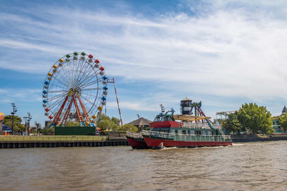 A catamaran on the river passing in front of Parque de la Costa and its Ferris wheel
