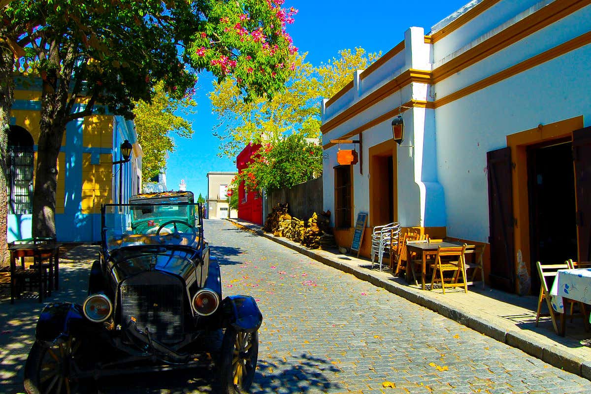 Una calle empedrada de Colonia del Sacramento, con un coche antiguo y varias mesas de restaurantes vacíos