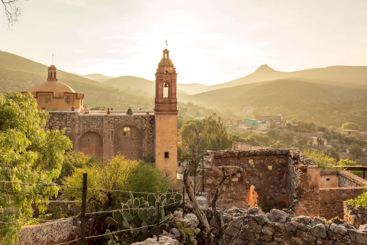 Iglesia antigua y varias casas en ruinas rodeadas de un cerro al atardecer