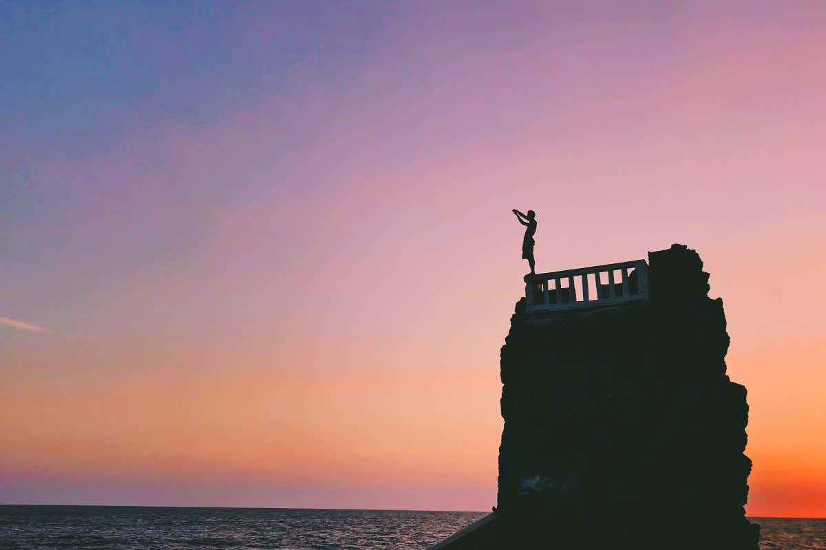 Un clavadista saltando desde lo alto de una roca hacia el mar al atardecer