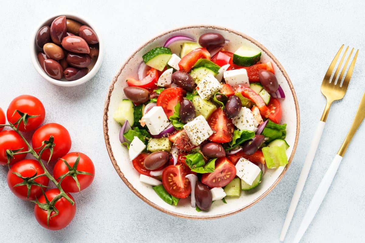 Plato con una ensalada griega junto a una rama de tomates cherry y aceitunas