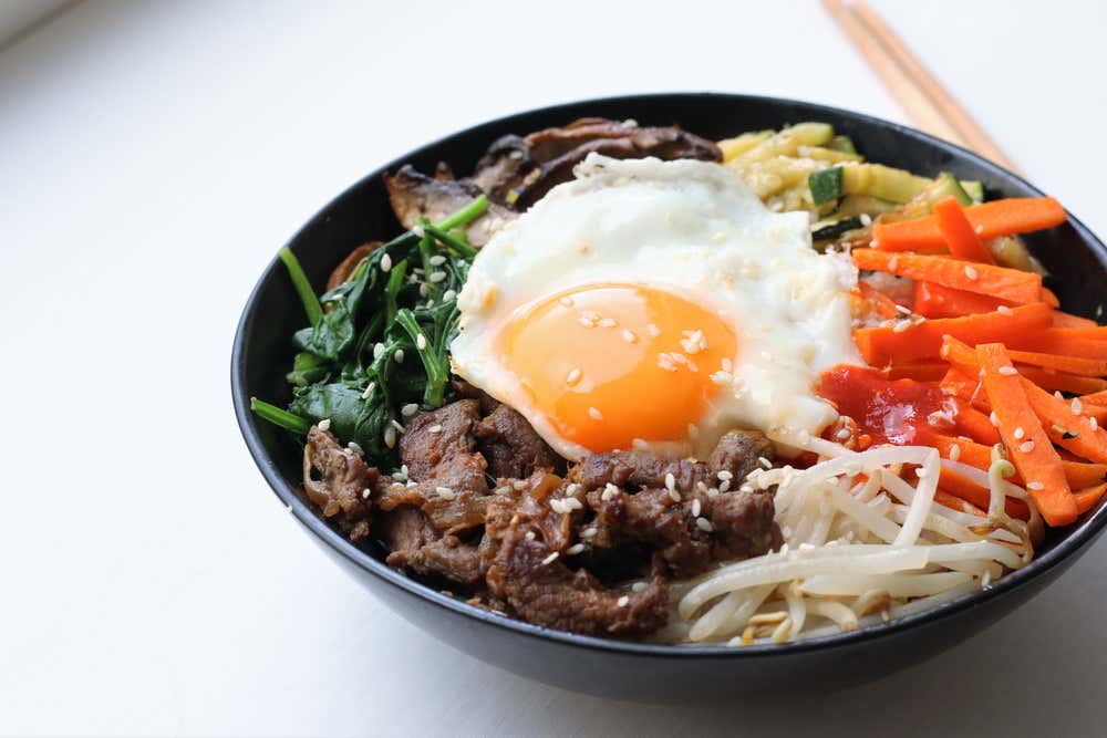 Detalhe de uma tigela com ovo frito, cenoura, carne picada, repolho e outras verduras refogadas