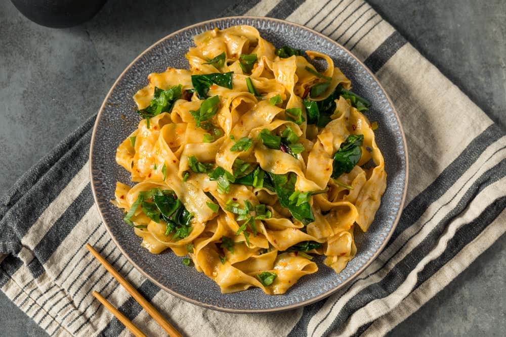 Detalhe de um prato de macarrão Biang Biang caseiro, com cebolinha, alho e sementes de gergelim em cima de um pano de prato