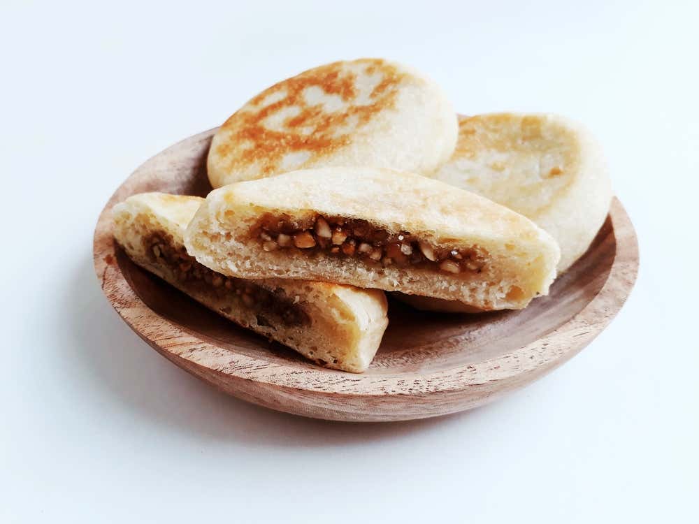 Hotteok, panquecas sul-coreanas, massa frita recheada com nozes e açúcar, comida tradicional de rua. É servida em um prato de madeira com fundo branco