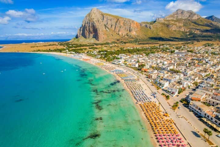 Vista dall'alto sulla spiaggia cittadina di San Vito lo Capo, con stabilimenti balneari, ombrelloni colorati e bagnanti nell'acqua turchese del mare della Sicilia