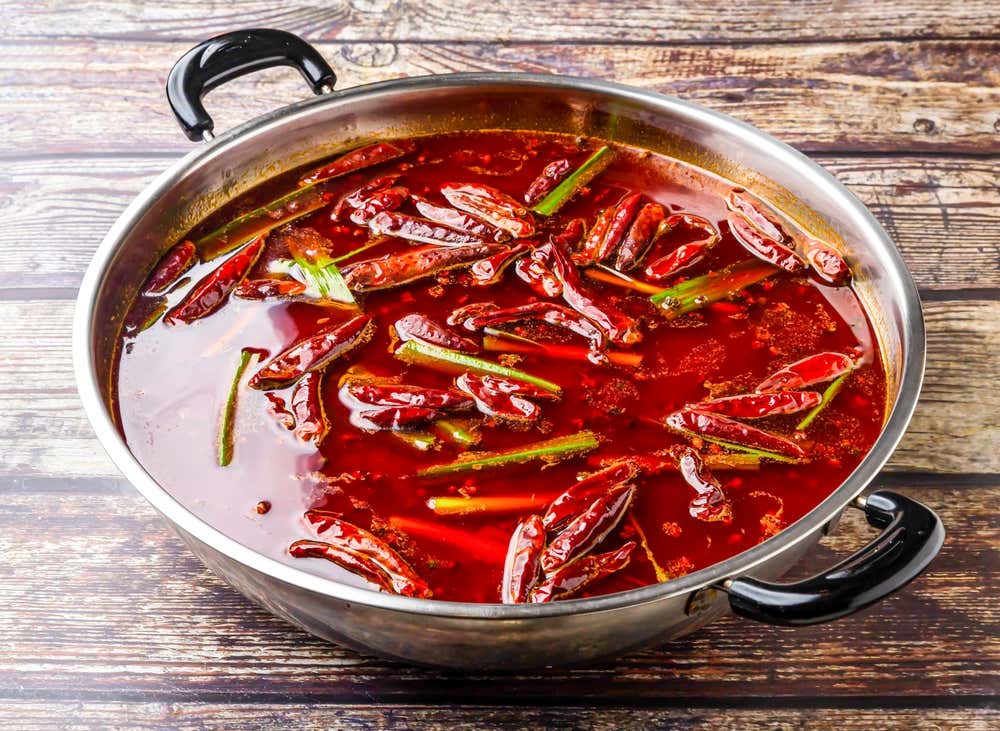 Hot pot picante de Sichuan servido em uma panela de aço, preparado com pimentas e cebolinha, um prato tradicional da culinária chinesa apresentado sobre uma mesa de madeira