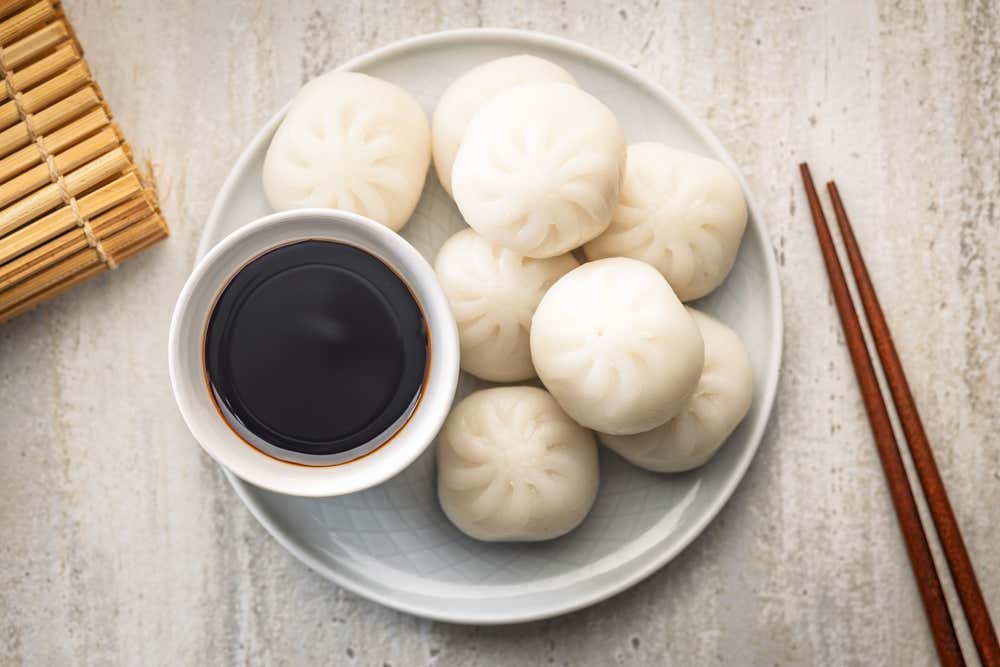 Detalhe de um prato de Xiaolongbao, tradicionais bolinhos da culinária chinesa, com um pouco de molho de soja ao lado