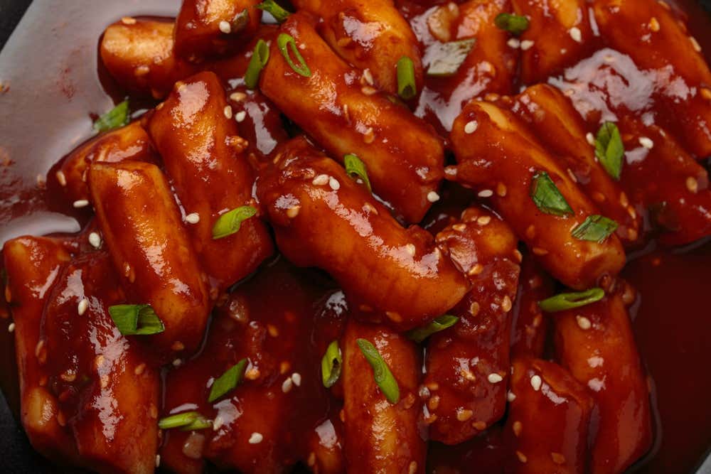 Detalhe do tradicional tteokbokki coreano servido com sementes de gergelim sobre um fundo preto rústico