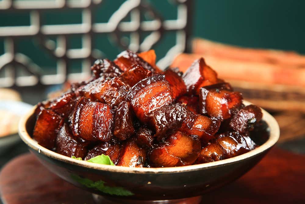 Panceta de porco Dongpo servida em uma tigela de cerâmica, preparada lentamente com molho de soja e vinho até adquirir uma textura macia e uma cobertura caramelizada brilhante, um prato clássico da culinária de Hangzhou, na China