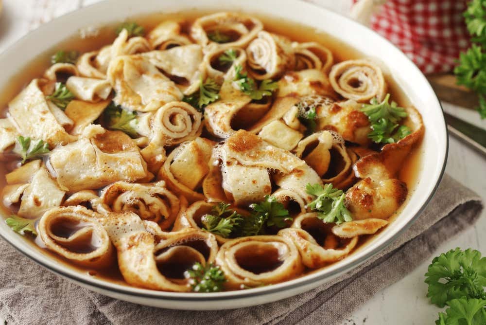 na ciotola di Frittatensuppe, una zuppa austriaca tradizionale, piena di brodo trasparente e numerose strisce di frittata arrotolate e tagliate sottilmente, guarnita con prezzemolo fresco tritato