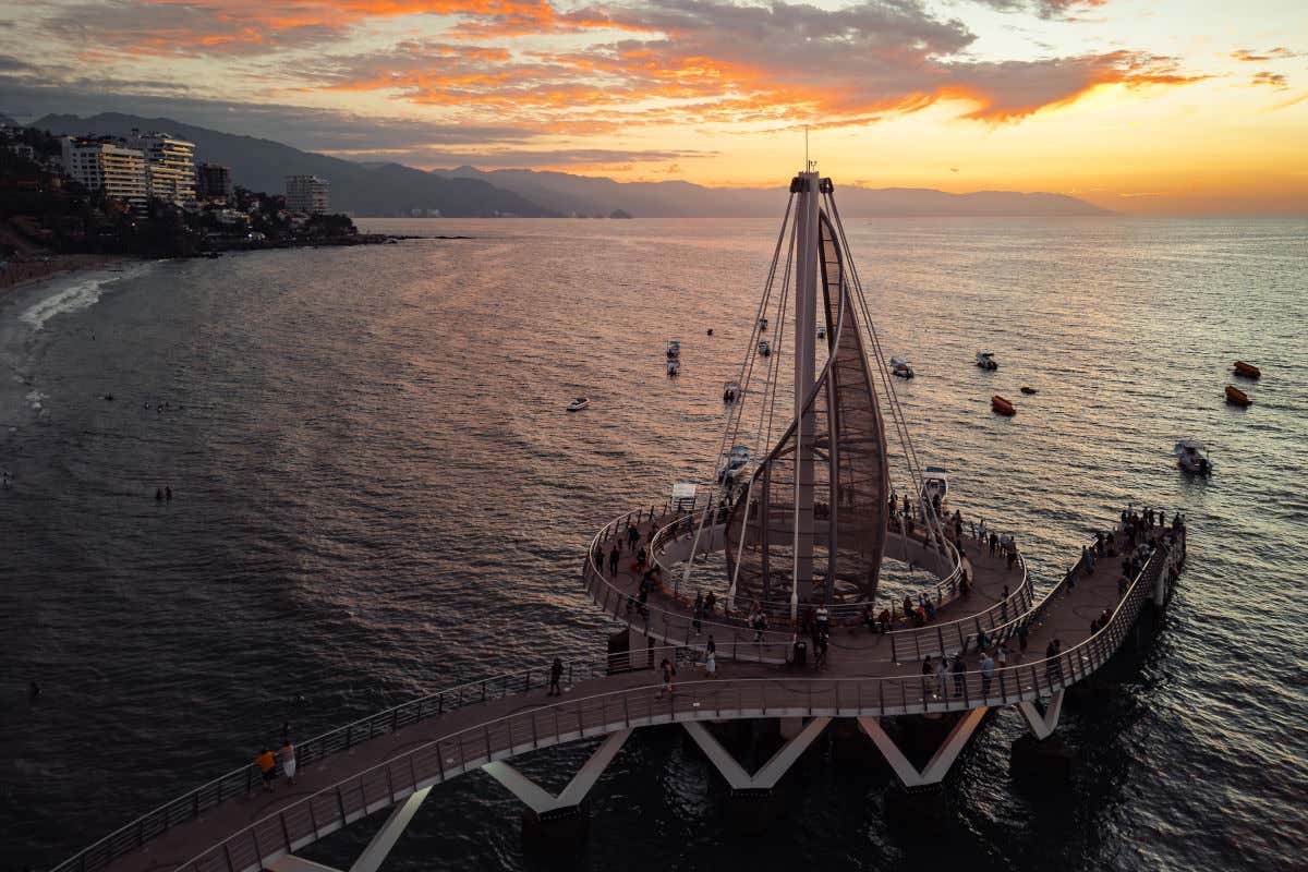 Atardecer en Puerto Vallarta visto desde un muelle junto a una playa y varias montañas
