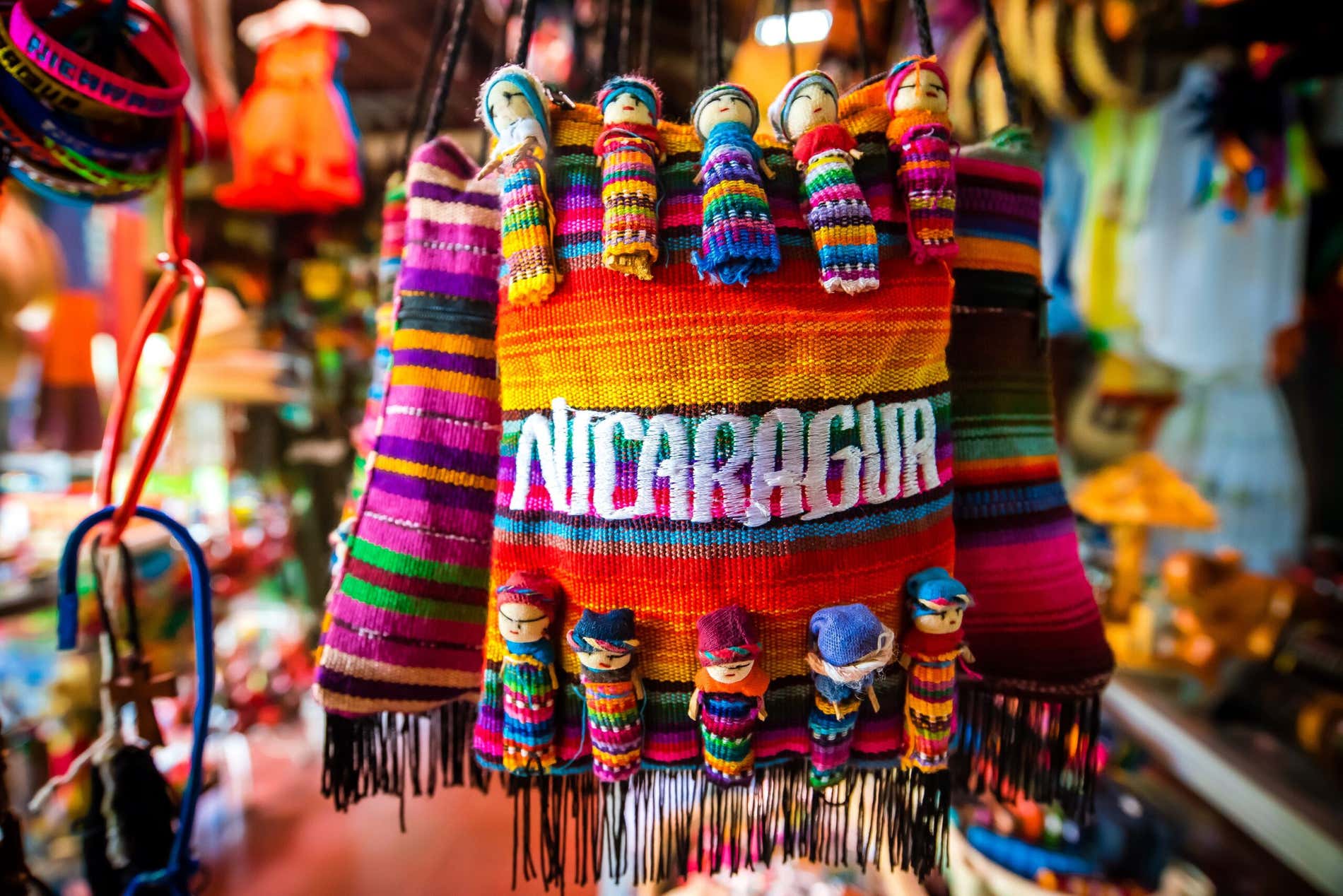 Bolso textil colorido con la palabra Nicaragua y muñecos tradicionales en un puesto de Masaya