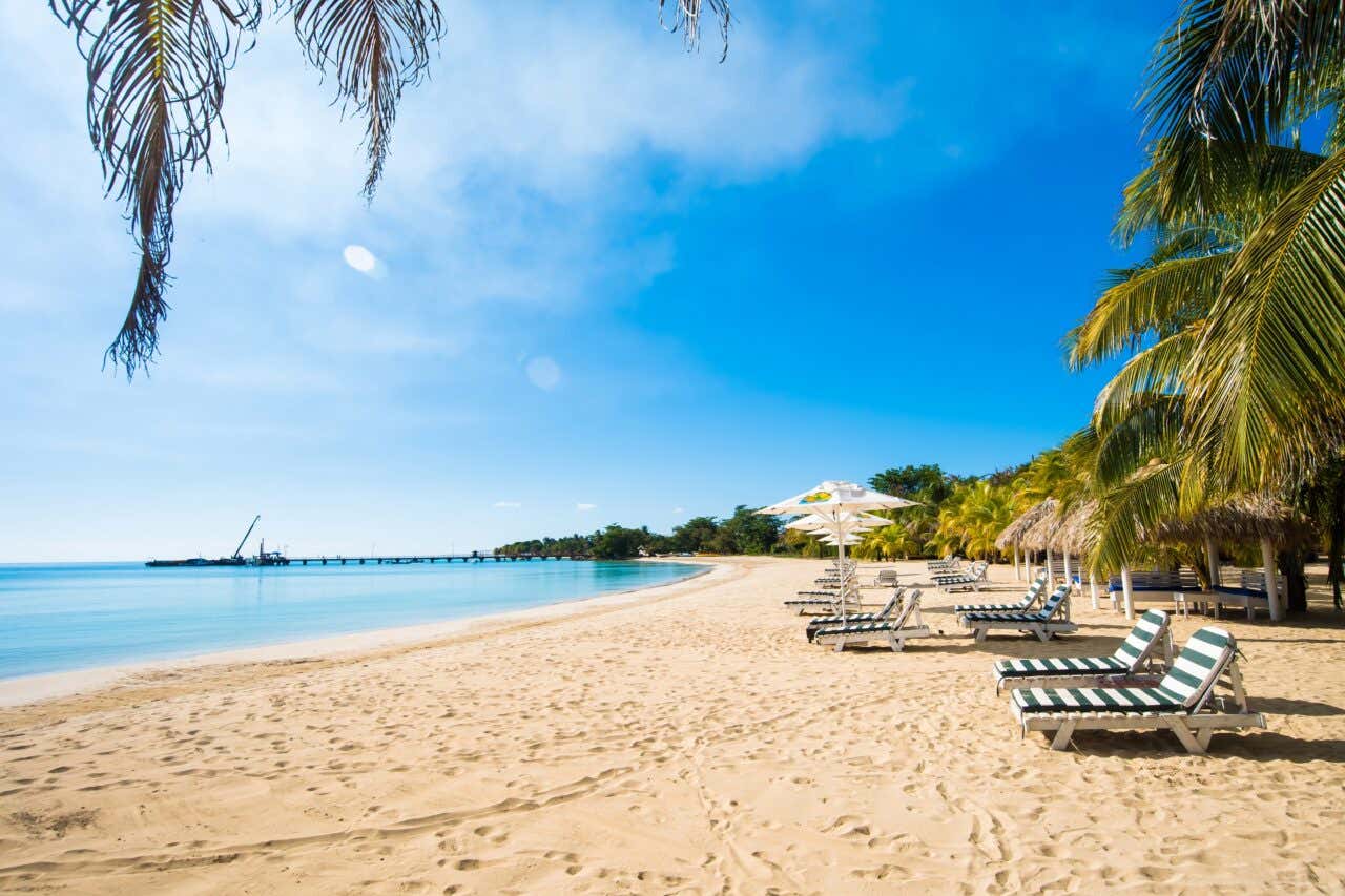 Playa paradisíaca de arena blanca con tumbonas, sombrillas y palmeras frente al mar en Corn Island