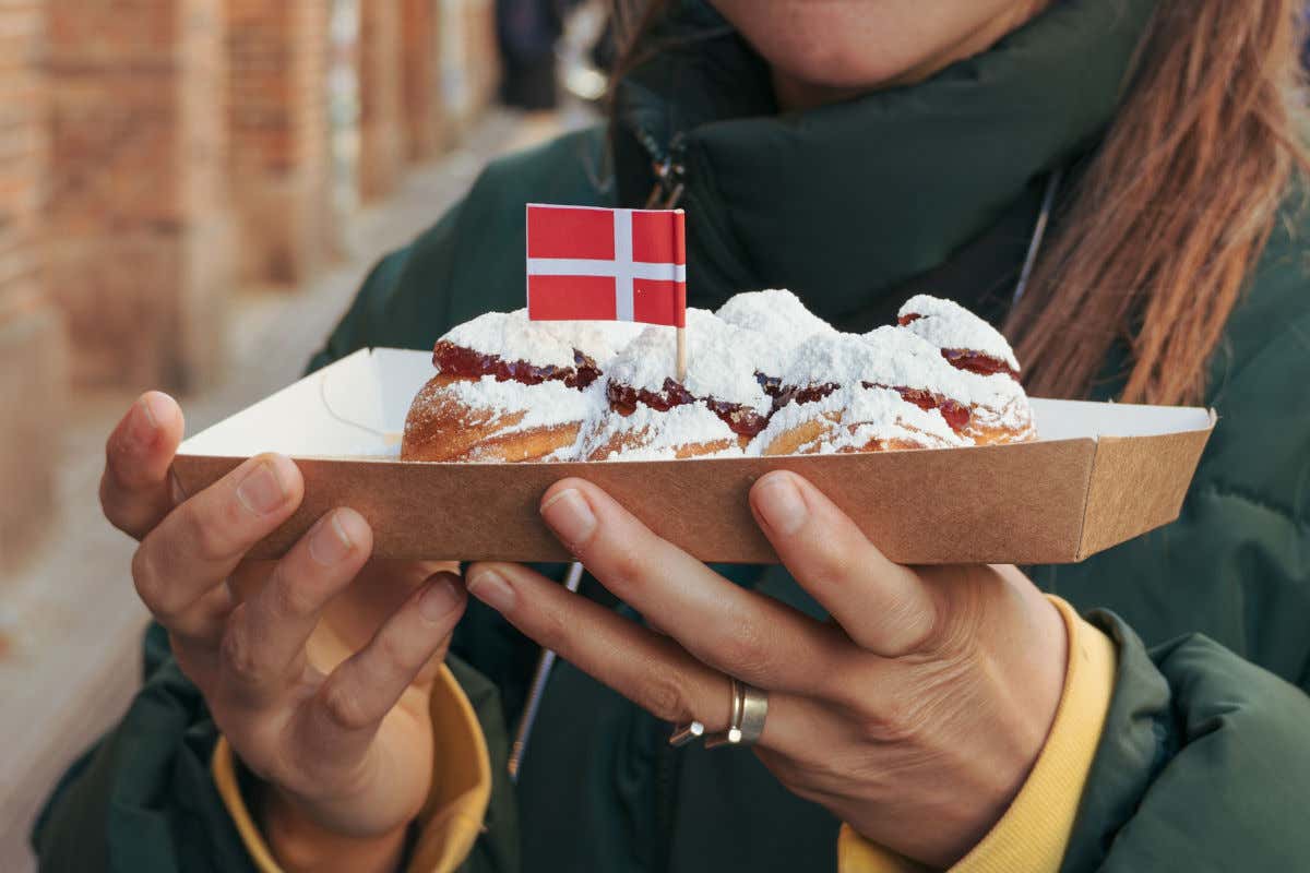 Unas manos de mujer sujetando unos Æbleskiver, unos bollos esponjosos espolvoreados con azúcar glas y típicos de Dinamarca en Navidad