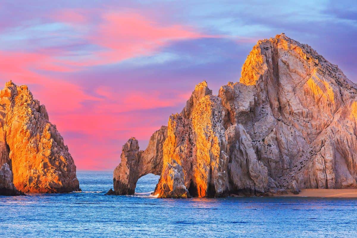 El Arco in Los Cabos as seen during a sunset with a pink sky in the background.